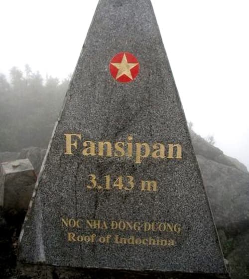 Mountain summit plateau with stone markers, rocky terrain, and panoramic views of surrounding peaks and valleys