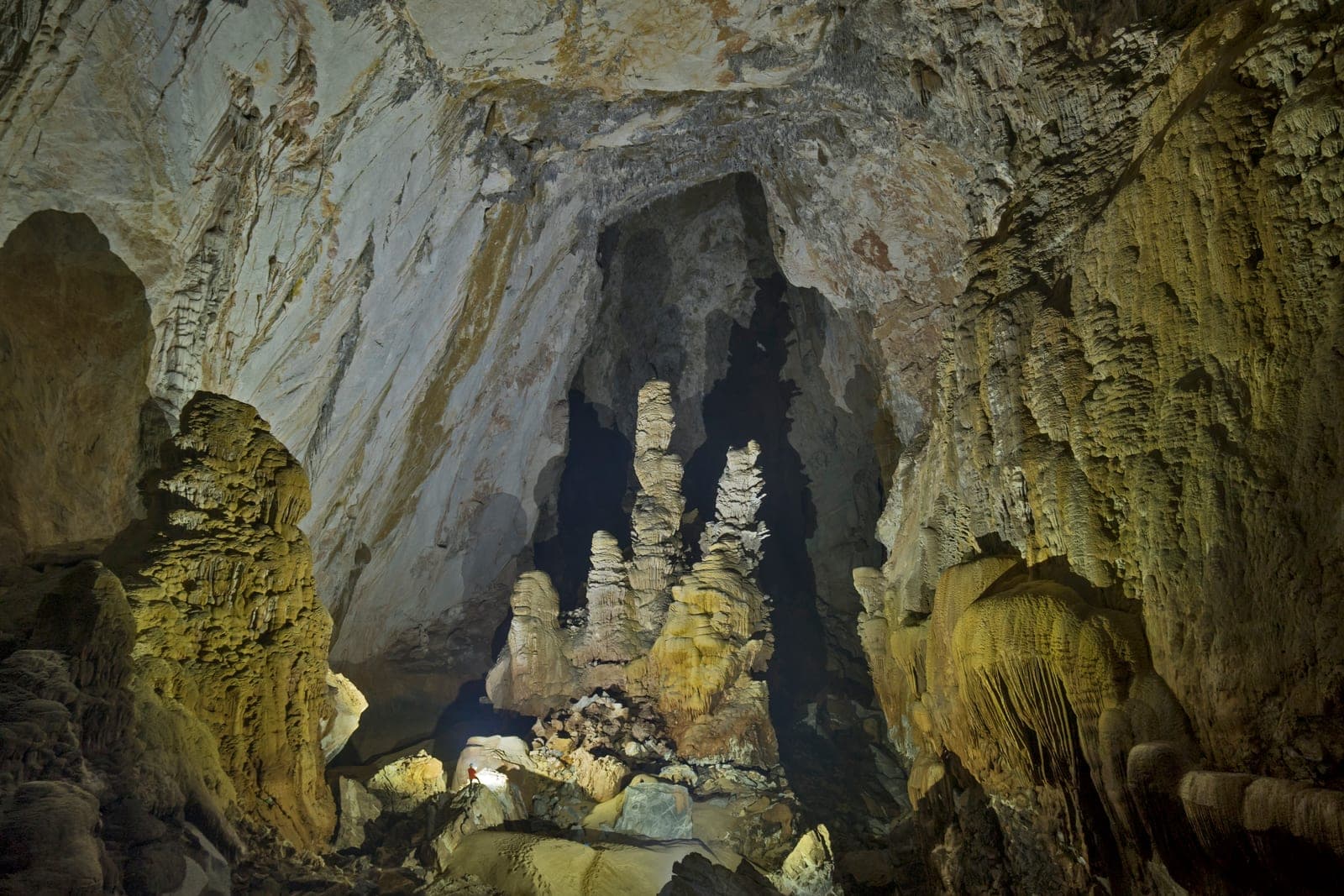 Massive stone cave chamber with towering entrance arch and interior river, showing geological limestone formations and cathedral-style light