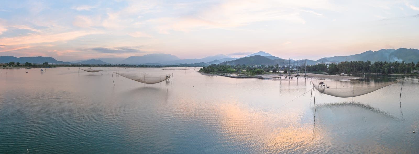 Wide view of the Cu Đê River in Da Nang with green water reflecting mountains and tropical vegetation along the banks.