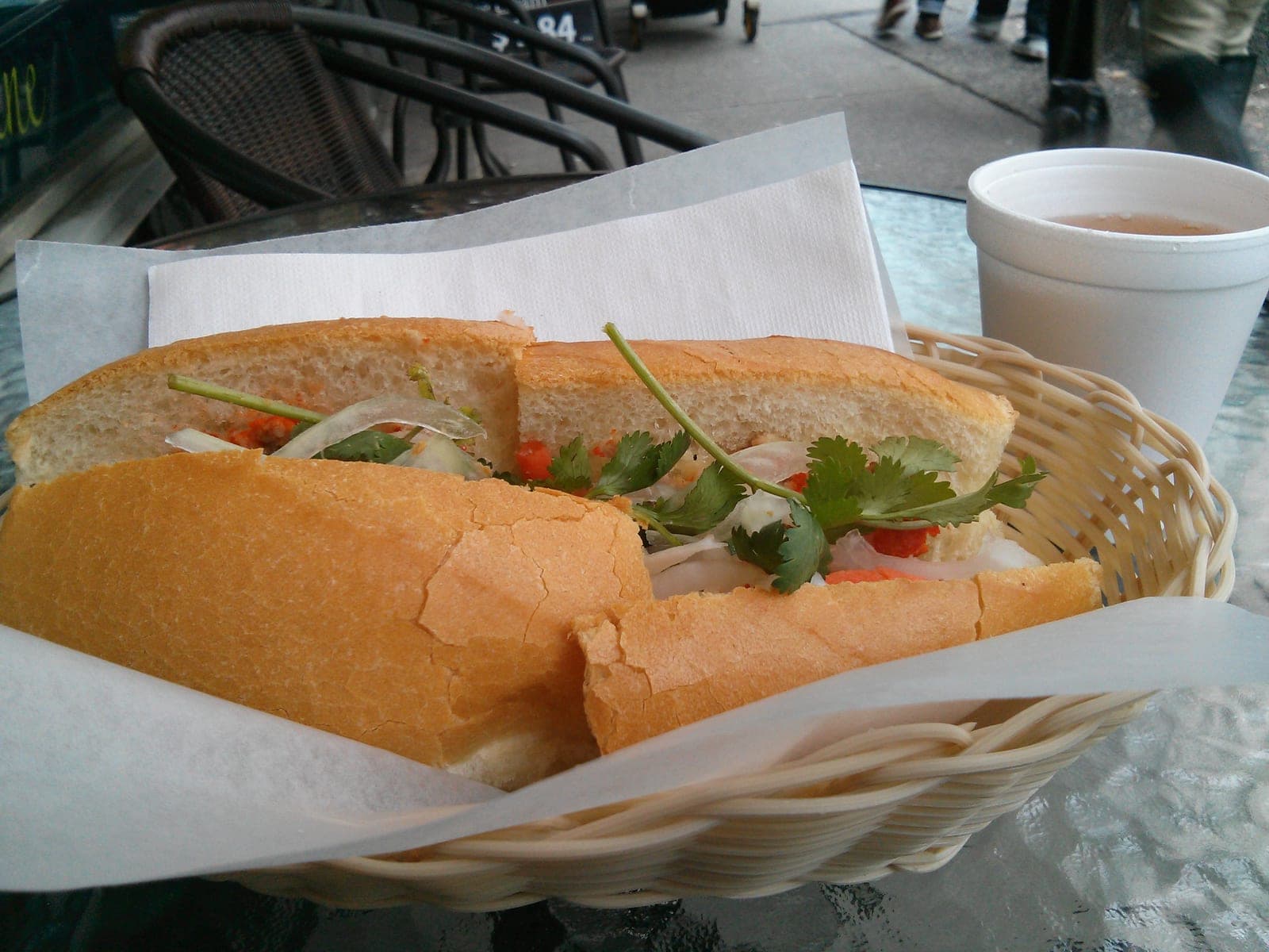 A fresh Vietnamese bánh mì sandwich cut in half, displaying crispy baguette, pâté, cold cuts, pickled vegetables, cucumber, and fresh herbs.