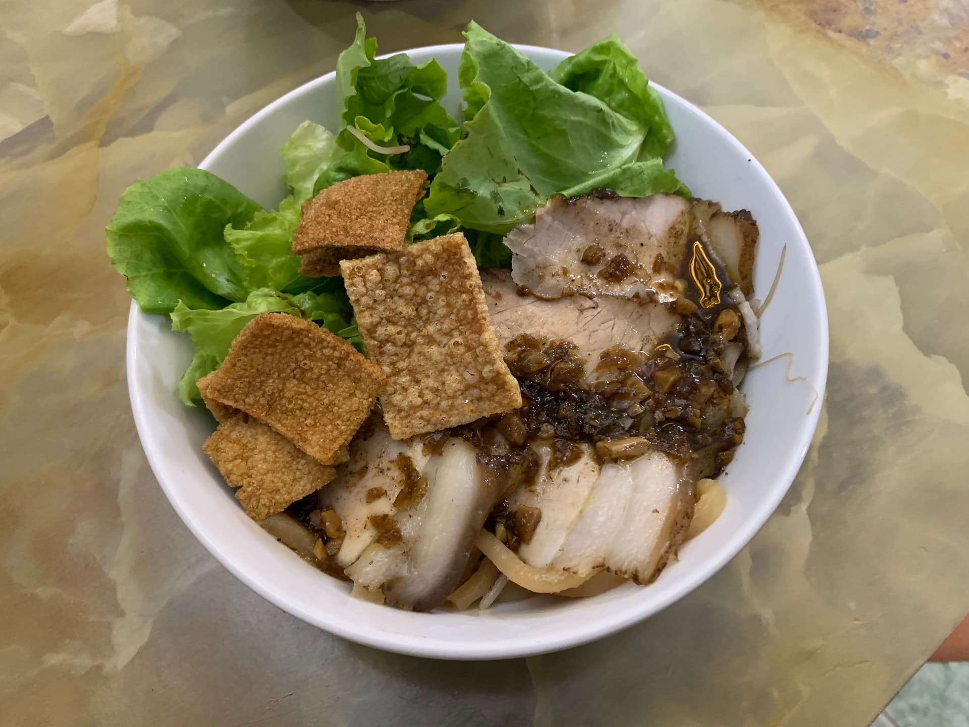 Bowl of cao lầu with thick noodles, char siu pork slices, fresh herbs, and fried noodle crackles