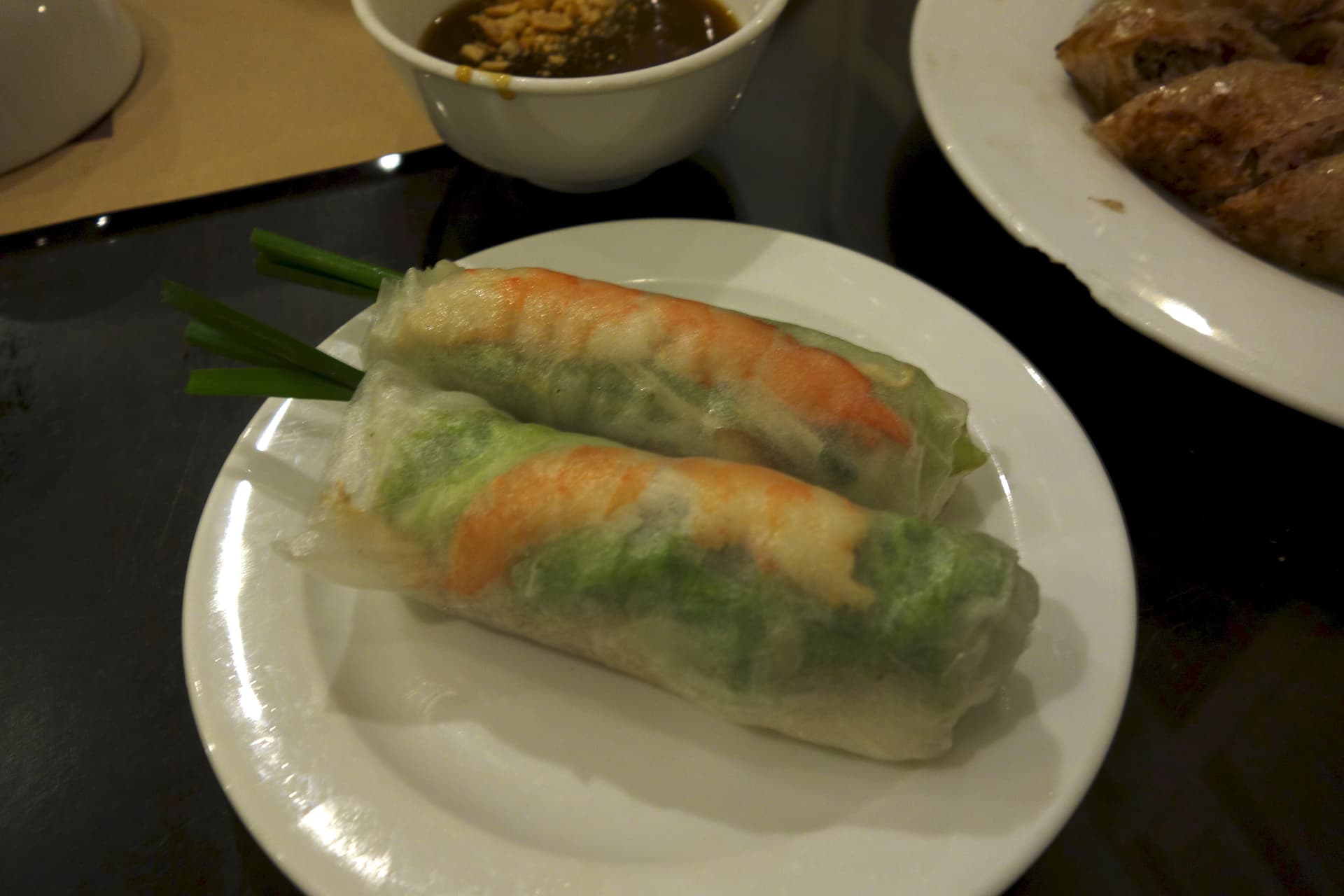 Transparent rice paper rolls filled with pink shrimp, herbs, and noodles arranged on a white plate