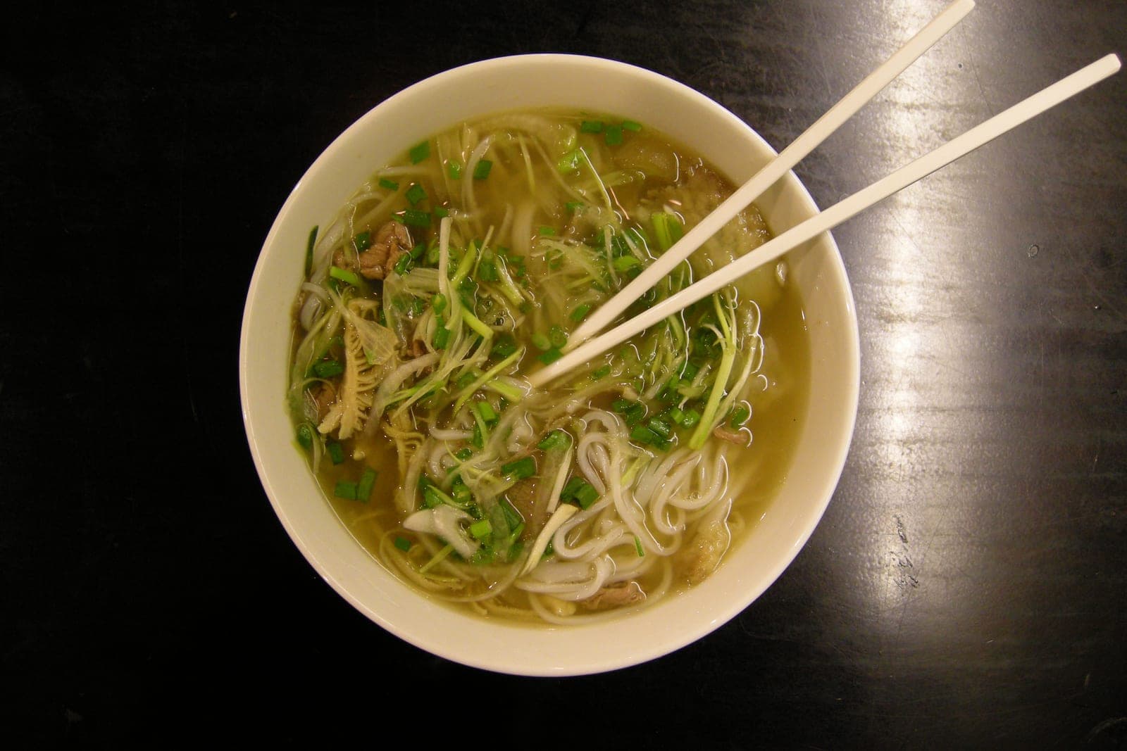 A steaming bowl of phở with clear broth, rice noodles, sliced beef, and fresh herb garnishes in Ho Chi Minh City