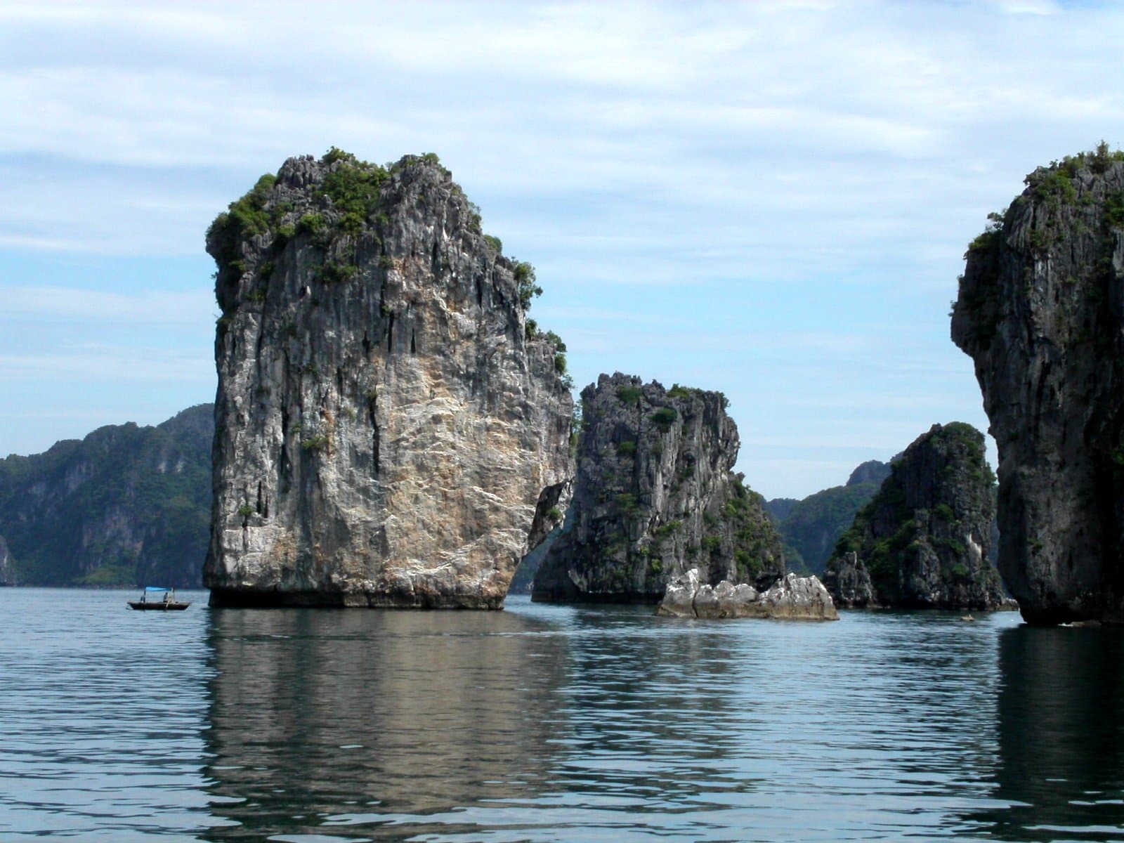 Towering limestone karst islands covered in lush vegetation rising from jade-colored water in Halong Bay, Vietnam