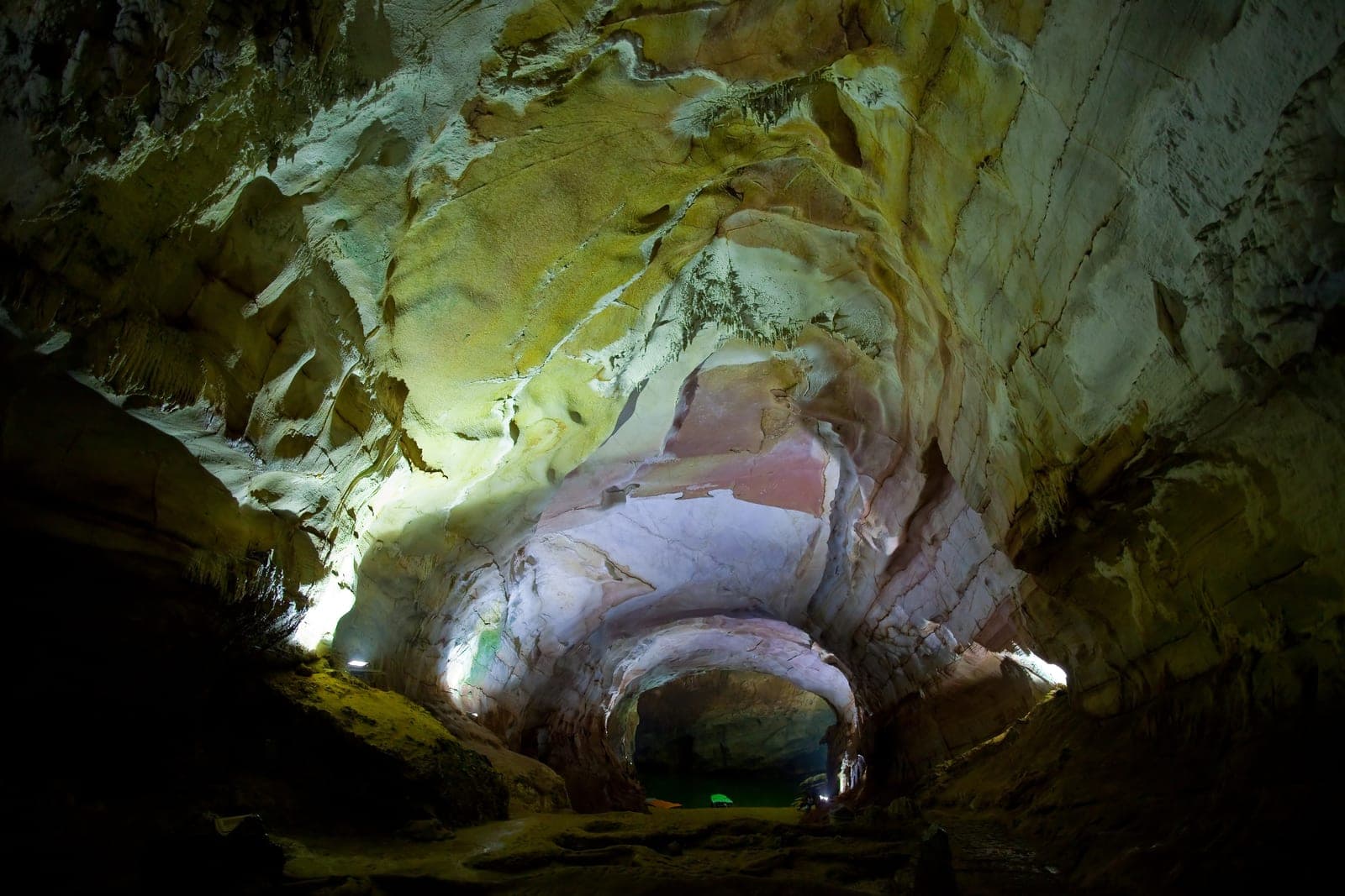 Limestone cave chamber with dramatic stalactites hanging from ceiling and underground river flowing through the passage.
