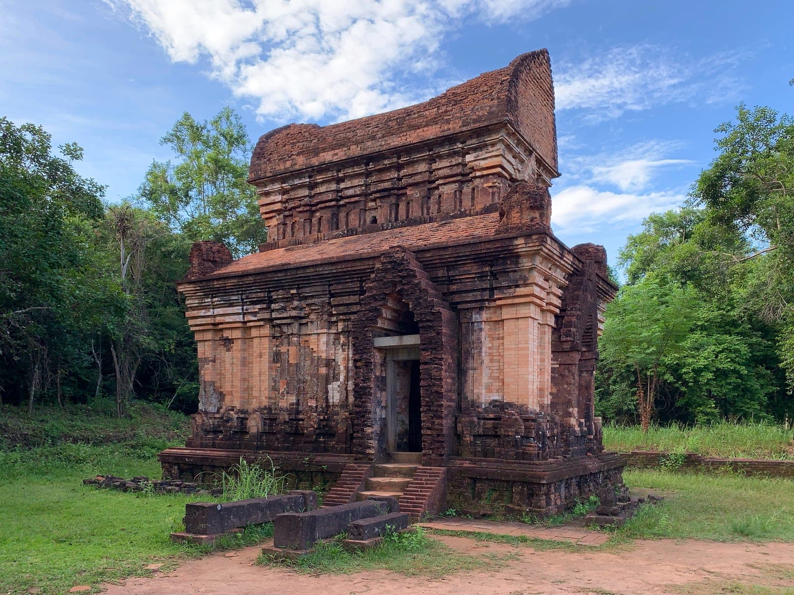 A deteriorated brick temple structure with intricate carved sandstone reliefs, part of the UNESCO-listed Mỹ Sơn Sanctuary temple complex.