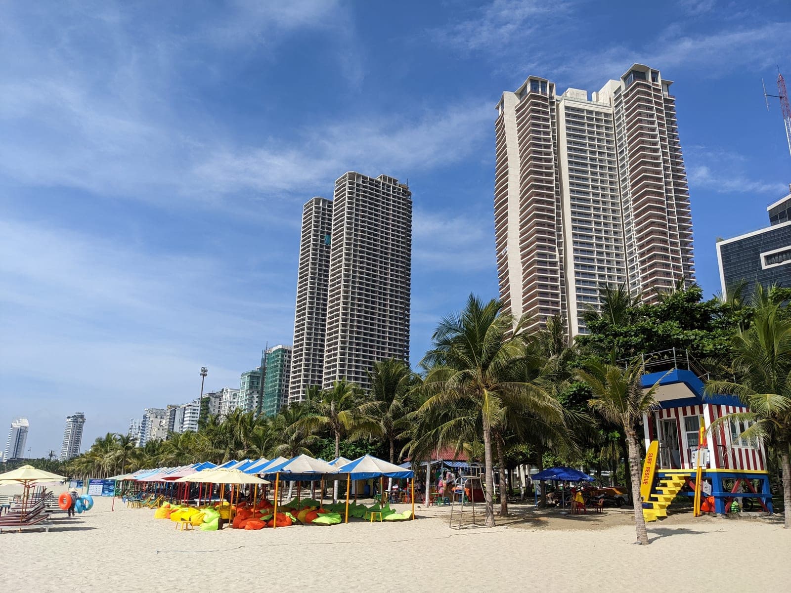 Golden sandy beach with high-rise resort buildings stretching along the coastline under clear blue skies