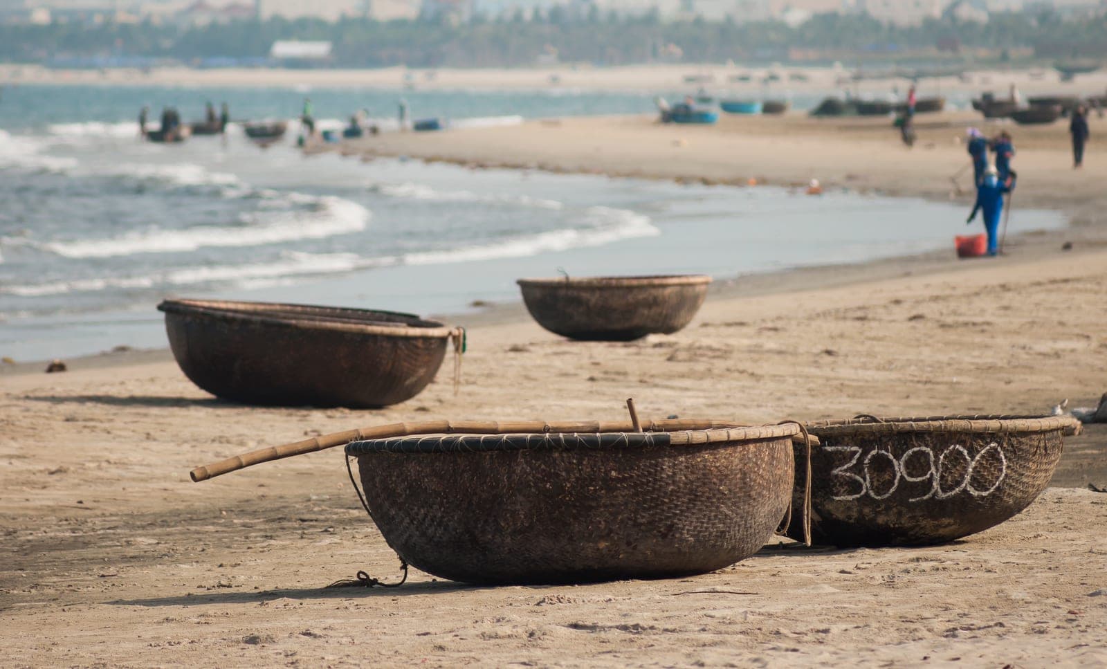 Traditional Vietnamese coracles lined up on Da Nang beach at sunrise with golden light reflecting off calm water