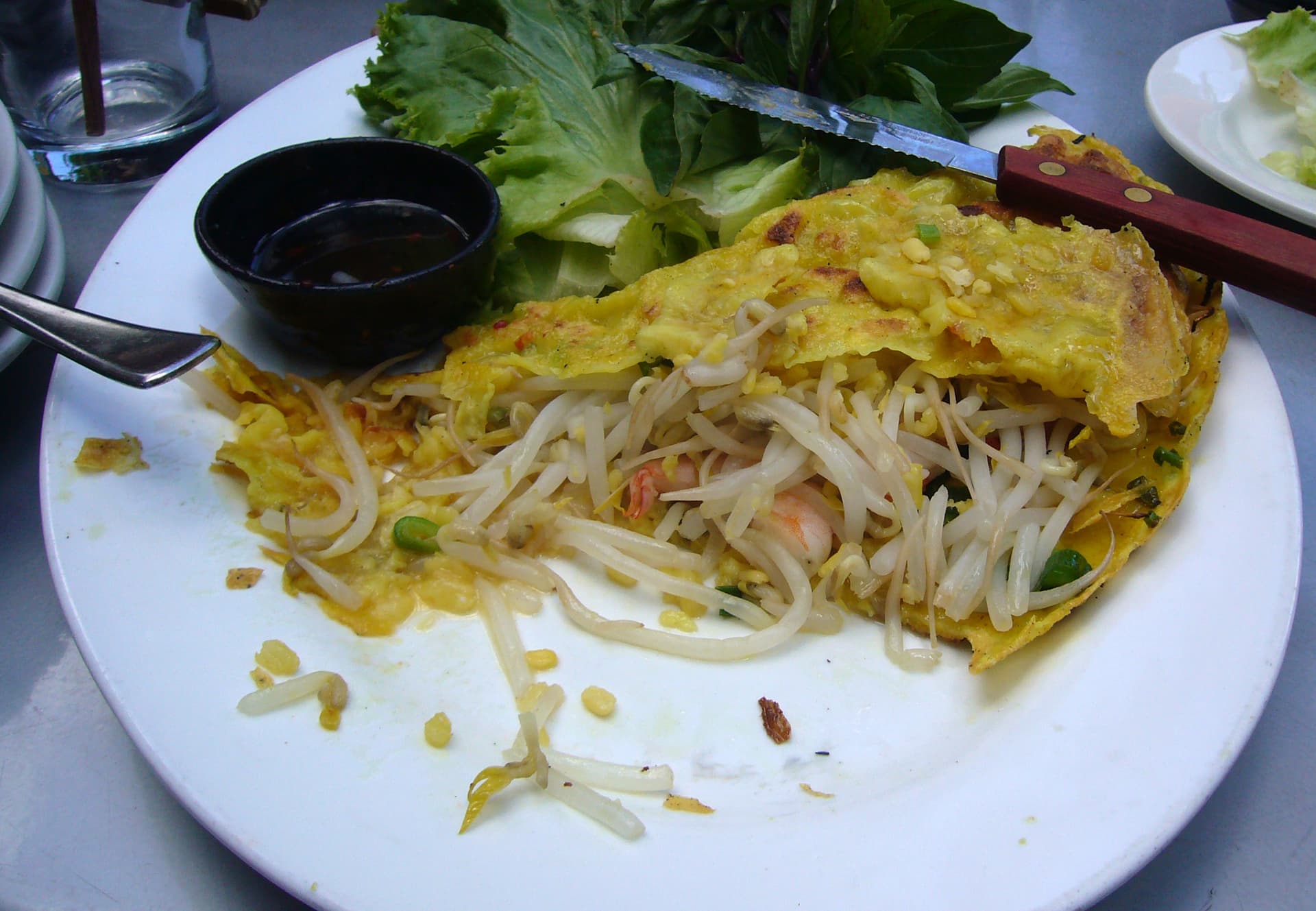Golden sizzling bánh xèo crepe folded on a plate, served with fresh herbs and lettuce for wrapping