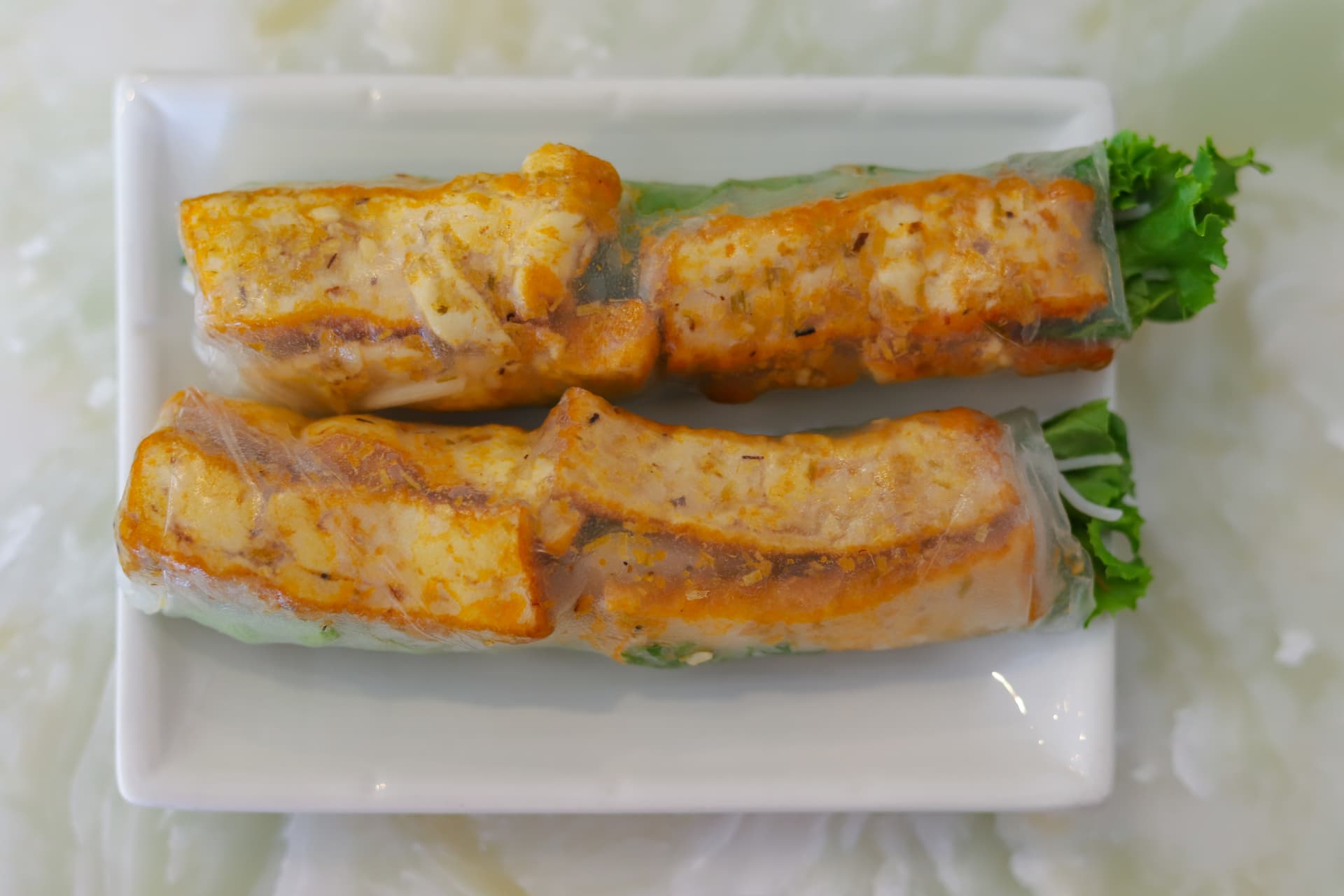 Fresh vegetarian spring rolls with translucent rice paper wrapper showing visible tofu and vegetables inside