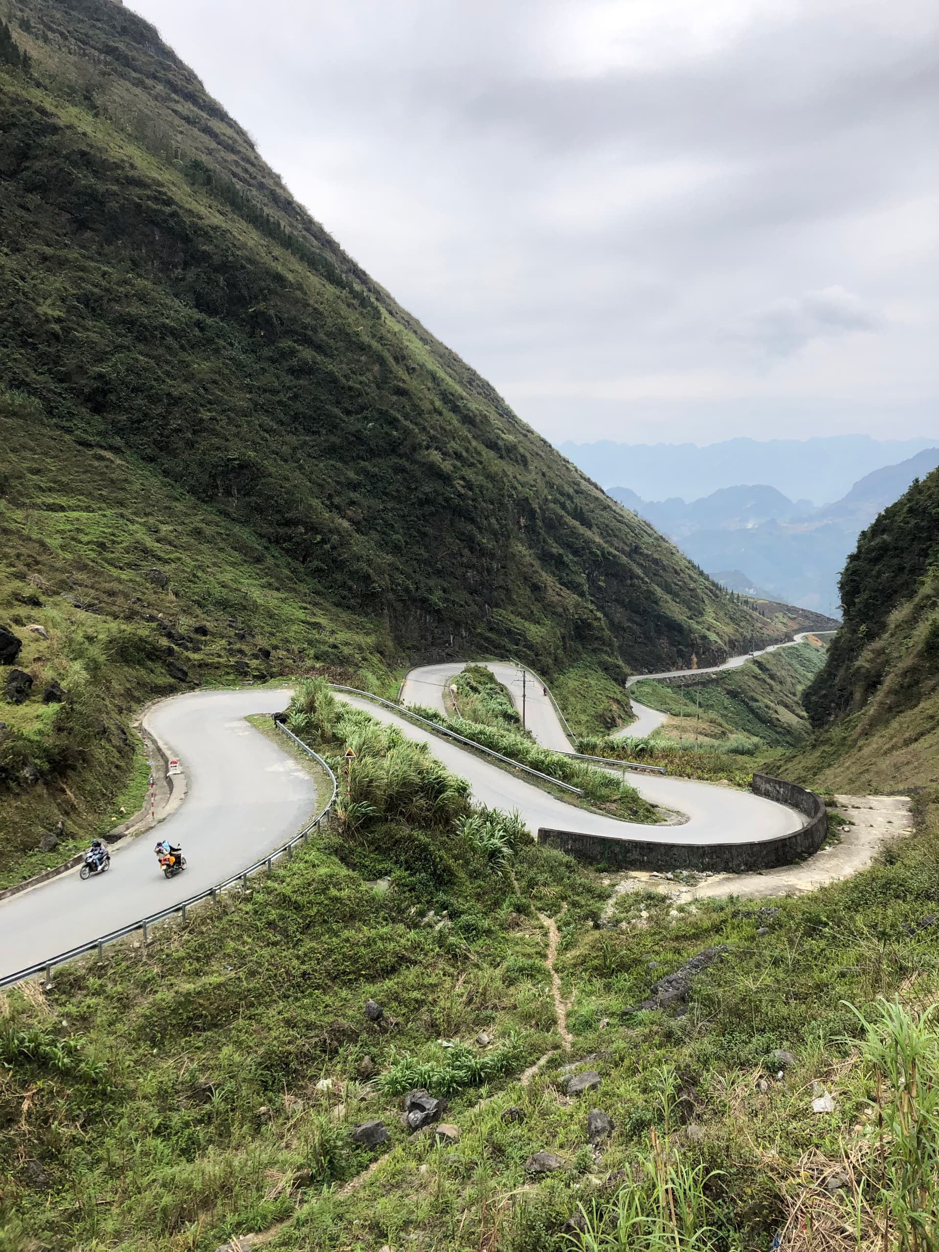 Winding mountain road carved into a limestone cliff face on the Ha Giang Loop with forested valleys visible below