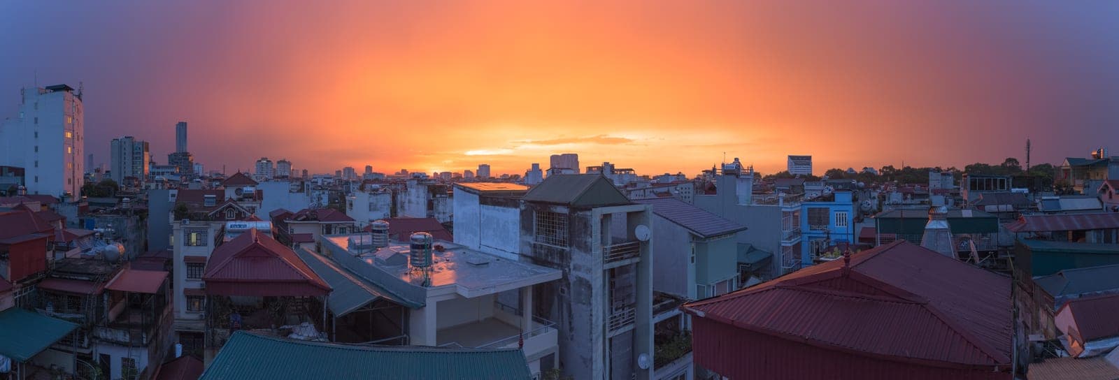 Hanoi cityscape at dusk with golden sunlight breaking through storm clouds after rainfall, illuminating wet buildings and streets below.